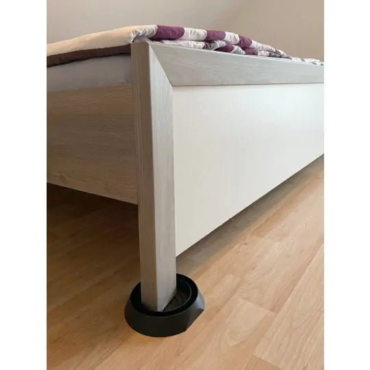 Das Bild zeigt ein helles Holzbett, dessen Bein in einer schwarzen Bettwanzen-Falle steht. Diese Falle dient zur Überwachung und Vorbeugung, indem sie verhindert, dass Bettwanzen unbemerkt ins Bett gelangen. Durch die Platzierung an allen Bettbeinen lassen sich Befälle frühzeitig erkennen und effektiv eindämmen. Die Methode ist diskret, kostengünstig und besonders für Privathaushalte, Hotels oder Ferienwohnungen geeignet.